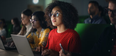 College age student sits in an auditorium environment looking up at a screen.