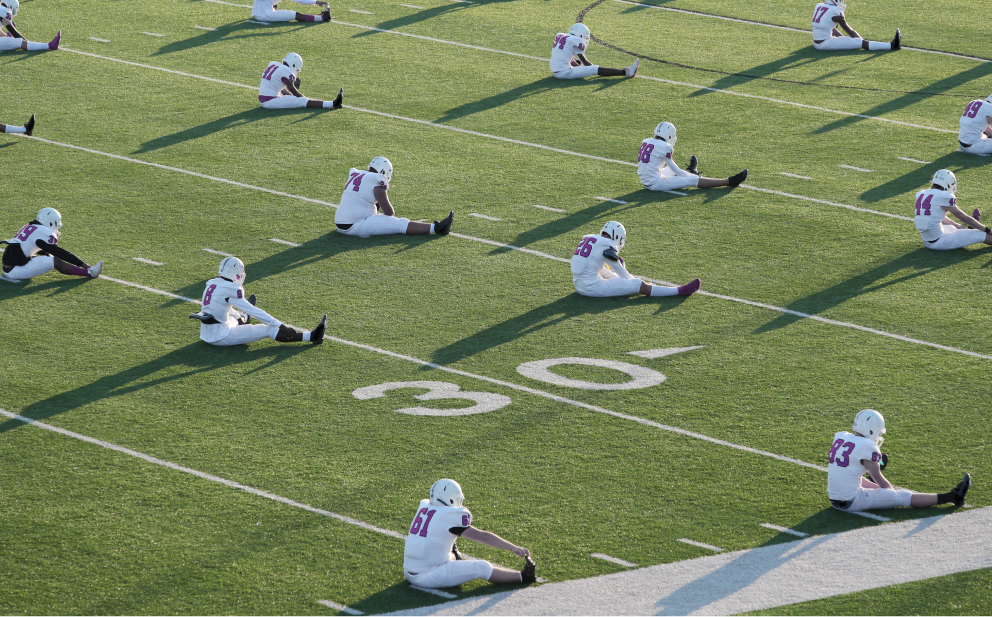 Seated football players engaging in pre-game stretching on the field