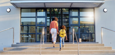 Adult woman accompanies child up steps into campus building